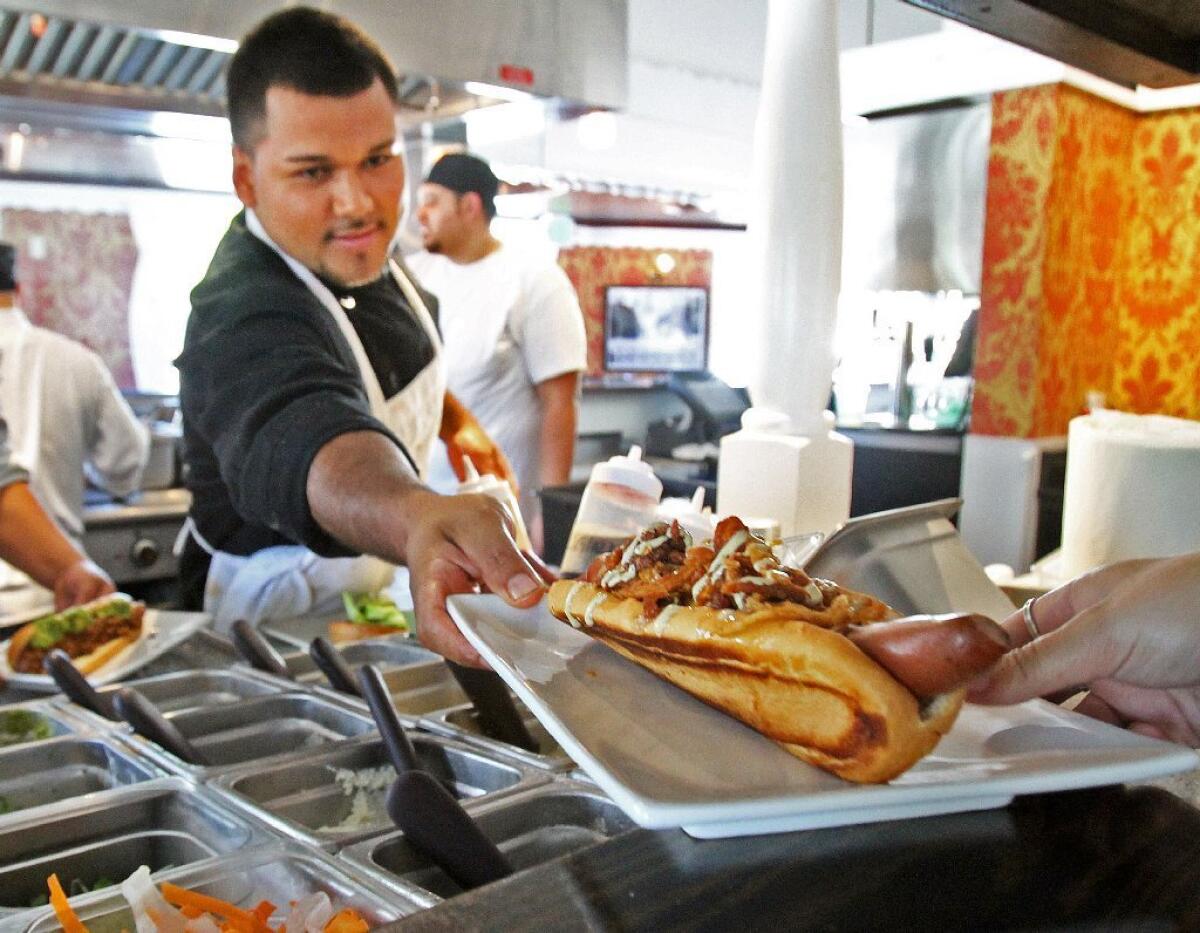 Eli Vargas hands a Manly Dog out to a server at Umami Burger in Burbank on Wednesday, July 31, 2013. Umami, which has been open nearly two weeks, moved into the location that was previously Papoo's Hot Dog Show. This Umami location serves hot dogs as a tip of the hat to the former restaurant, and it's the only one that serves them.