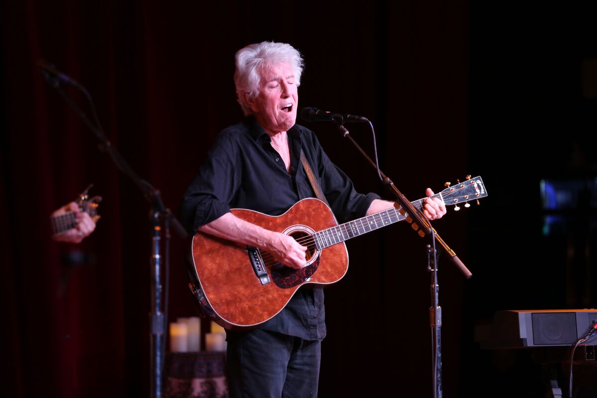 Graham Nash singing into a microphone and playing guitar