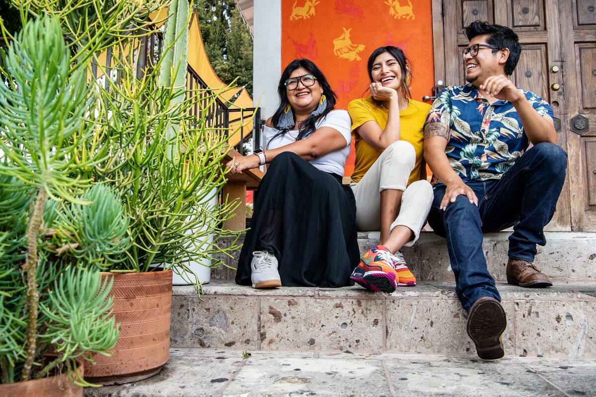 Two women and a man sit on a stoop with plants