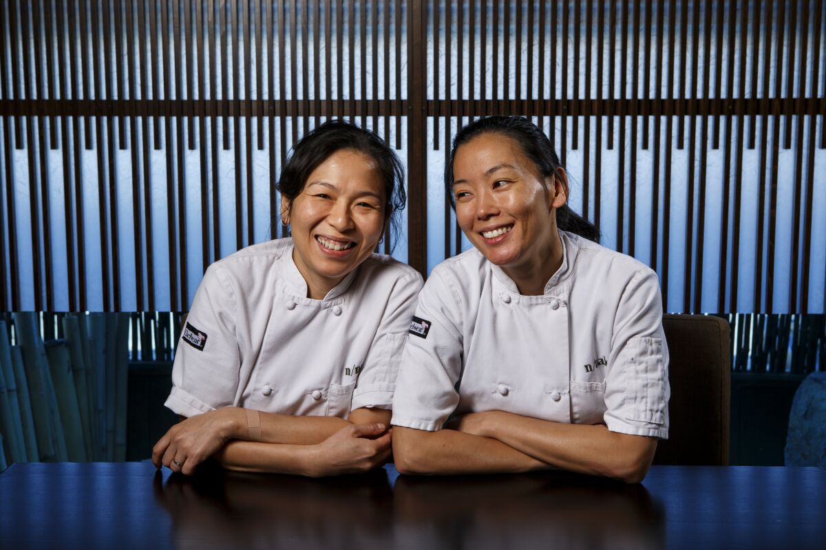 Two women in chef's whites, seated side by side at a table.