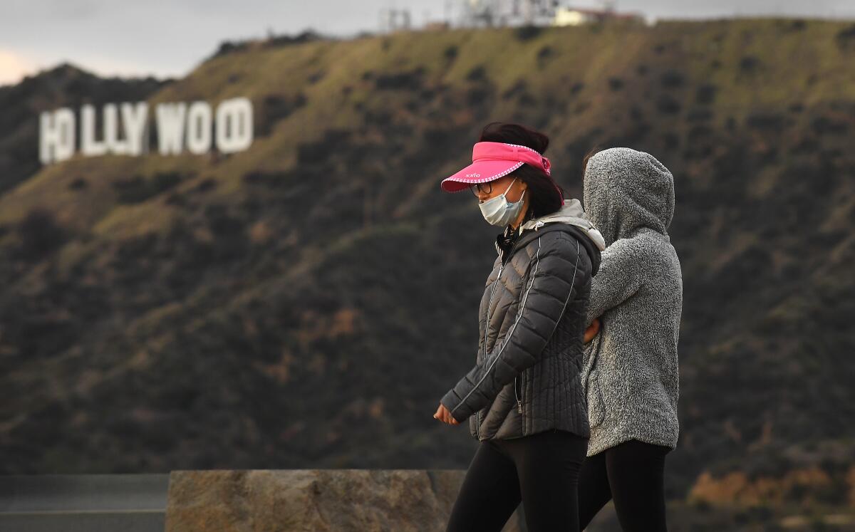 Hikers wearing masks because of coronavirus concerns walk past the Hollywood sign in Griffith Park on Monday.