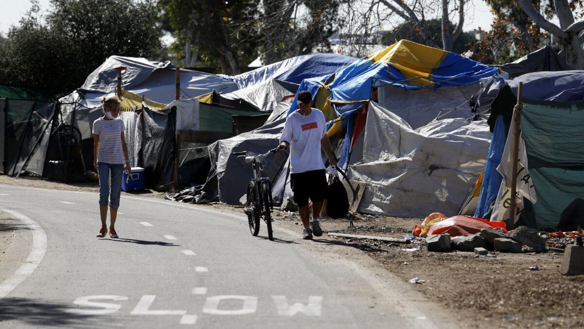 People walk past tents at a homeless encampment along the Santa Ana River trail in February in Anaheim. Orange County supervisors put forth a proposal Monday to move homeless people to temporary shelters in Irvine, Huntington Beach and Laguna Niguel.
