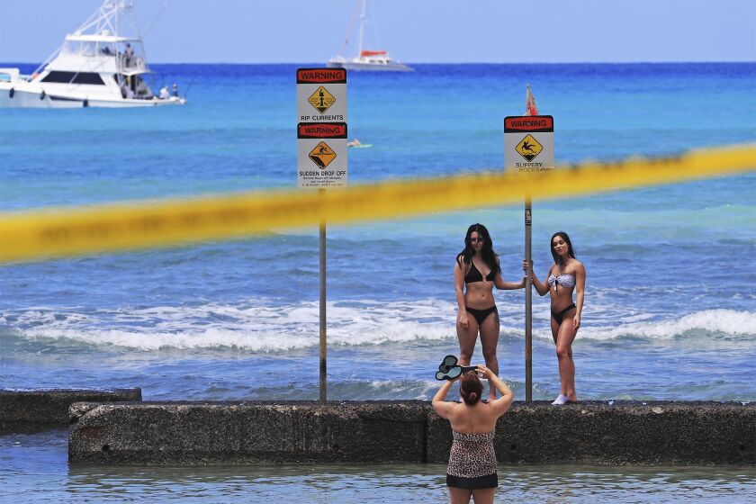 Beachgoers take pictures on a sea wall in Waikiki, Friday, March 20, 2020, in Honolulu. Honolulu closed all public parks and recreation areas Friday until the end of April in an effort to help stop the spread of the coronavirus. Yellow security tape wrapped across Waikiki as police and other officials informed beachgoers to leave the area. Many beachgoers simply went under the security tape to access the beach and shoreline. (AP Photo/Marco Garcia)