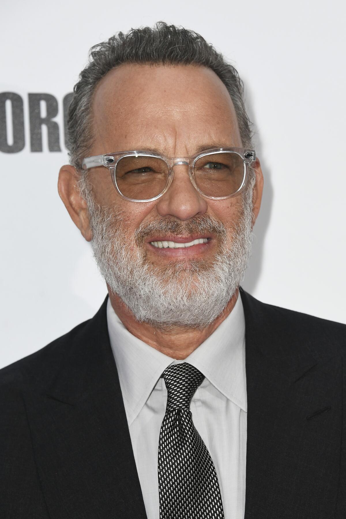 A man in a dark suit and light-framed sunglasses with a white beard. 