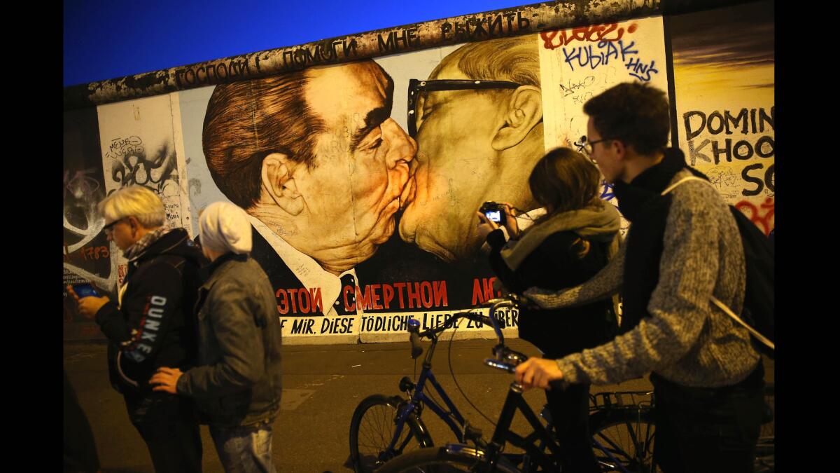 Visitors gather Oct. 28, 2014, at a mural showing former Soviet leader Leonid Brezhnev, left, kissing former East German communist leader Erich Honecker at the East Side Gallery, a section of the Berlin Wall that today is a tourist attraction.