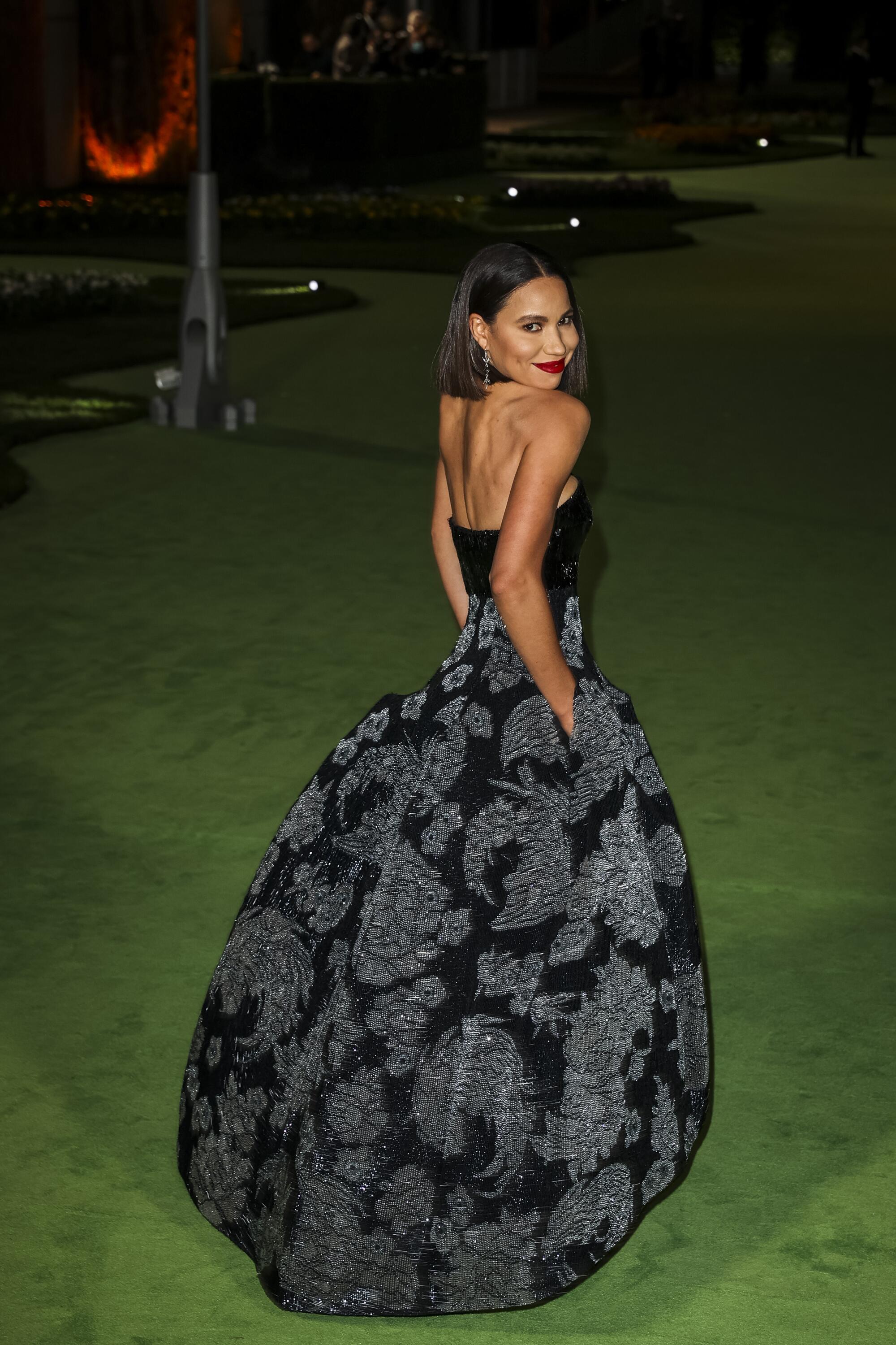 A woman in a patterned, black dress posing on a green carpet