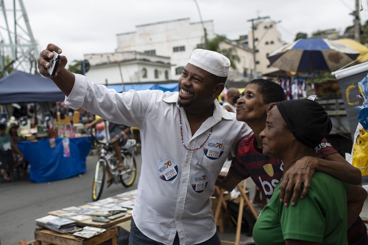 Wagner Luiz Abreu Machado, a priest from the Afro-Brazilian faith Umbanda who goes by Waguinho Macumba, takes a selfie with residents as he campaigns for a seat on the Sao Goncalo City Council with the Brazilian Social Democracy Party (PSDB) in Sao Goncalo, Rio de Janeiro state, Brazil, Sunday, Nov. 8, 2020. “No city councilor is committed to our causes,” Machado said, referring to the followers of African-influenced faiths. (AP Photo/Bruna Prado)