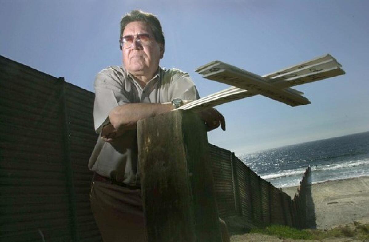 Migrant advocate Roberto Martinez, who became a full-time activist in the late 1970s, stands near a border fence with cardboard crosses to honor those who perished entering the United States.