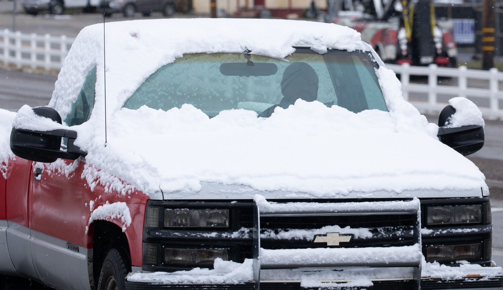 A motorist drives a pickup truck with its hood and roof covered in snow