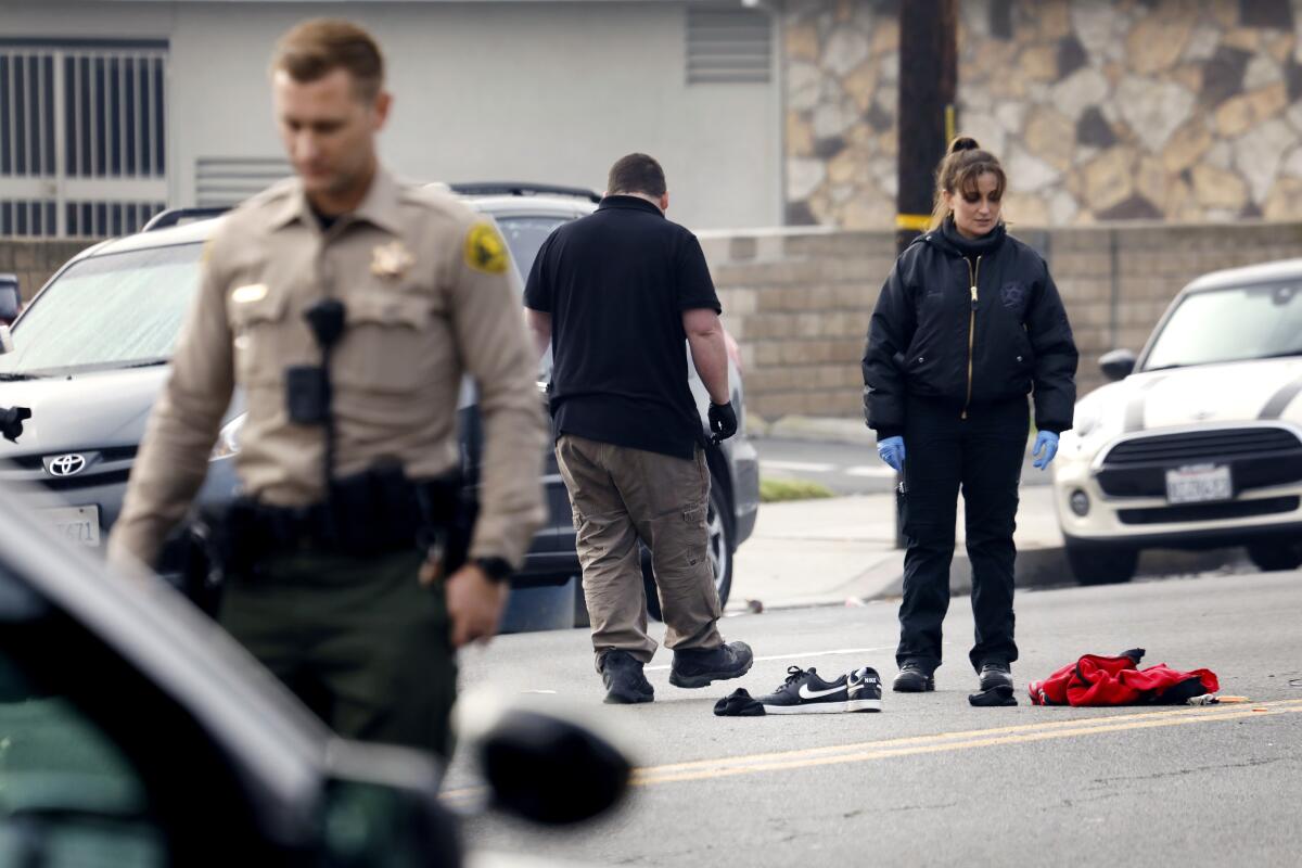 Three people stand in a street where Nike shoes and a red item of clothing also lie.