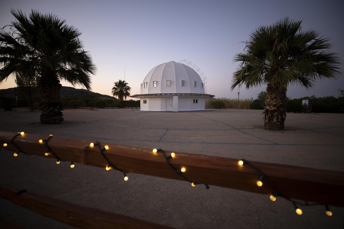 The domed Integratron at dusk, framed by two squat palm trees.