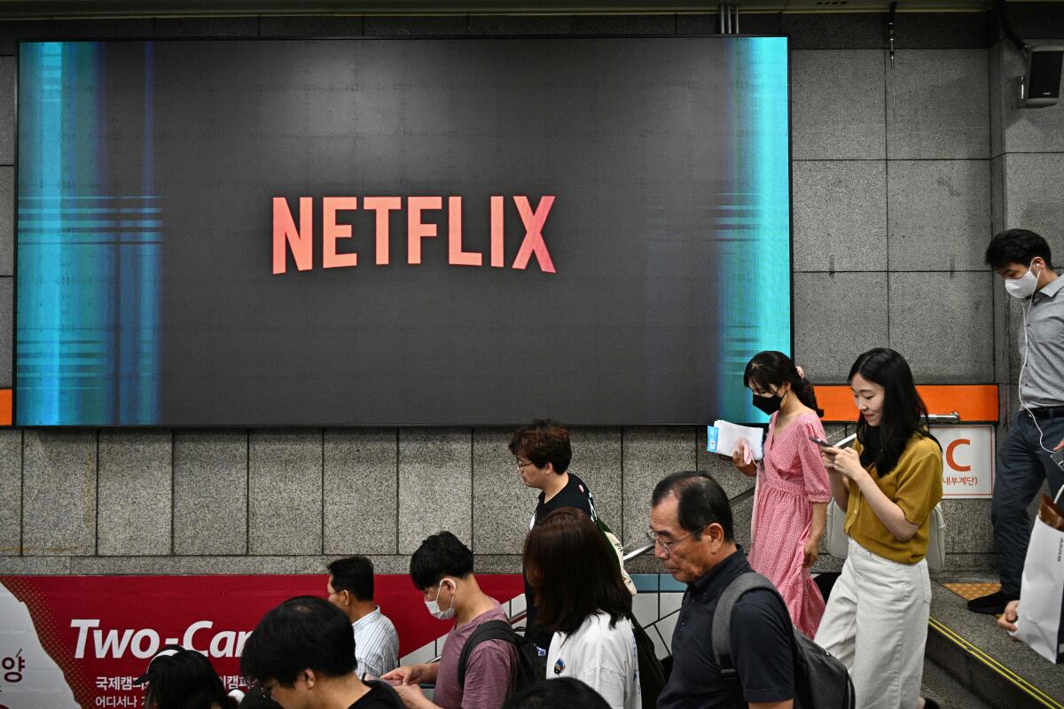 The Netflix logo is seen displayed on a digital monitor as commuters walk down a stairway in an underground metro station