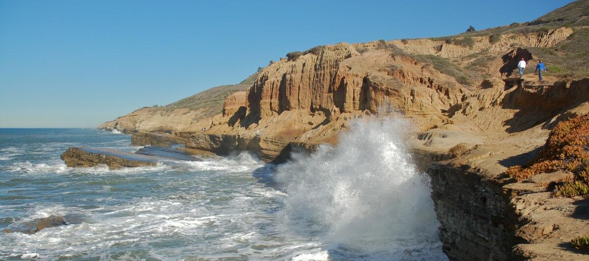 Waves batter the cliffs while two hikers pass at Cabrillo National Monument in Point Loma. Photo taken in 2010.