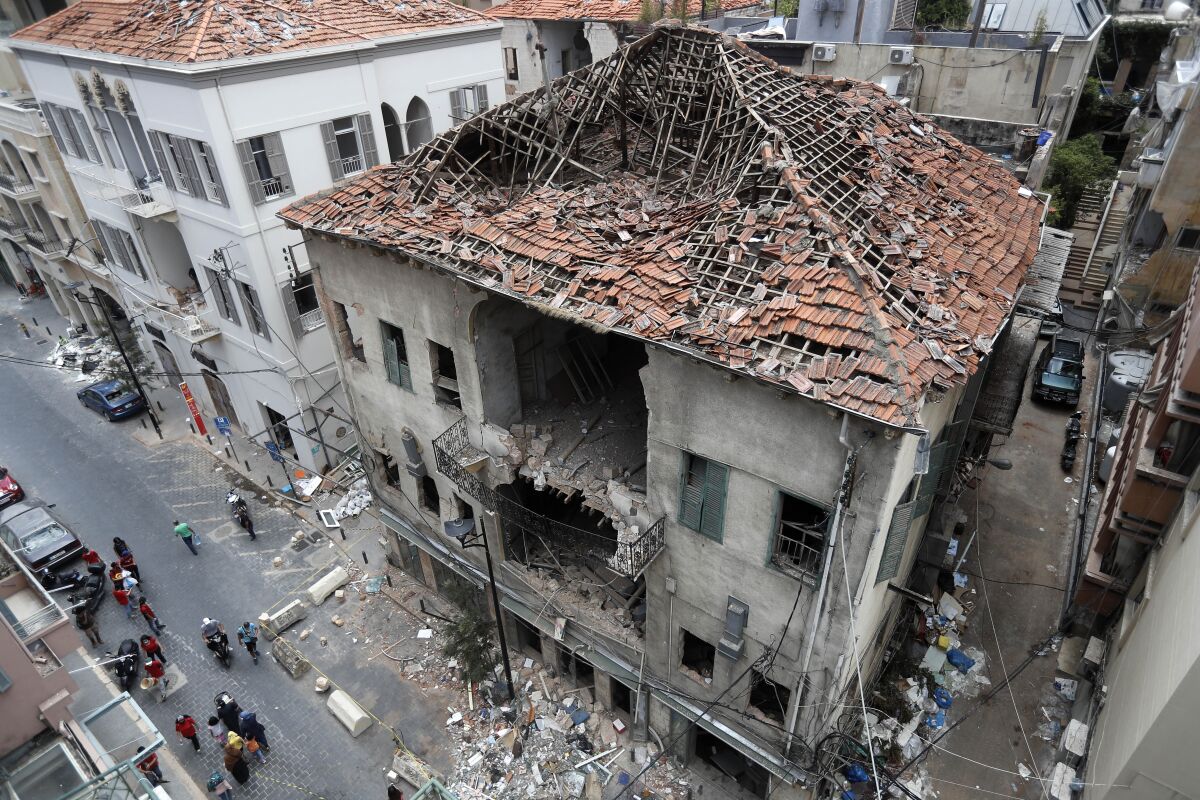 People pass in front of a house that was damaged during the last week's explosion that hit the seaport of Beirut, Lebanon, Tuesday, Aug. 11, 2020. (AP Photo/Hussein Malla)