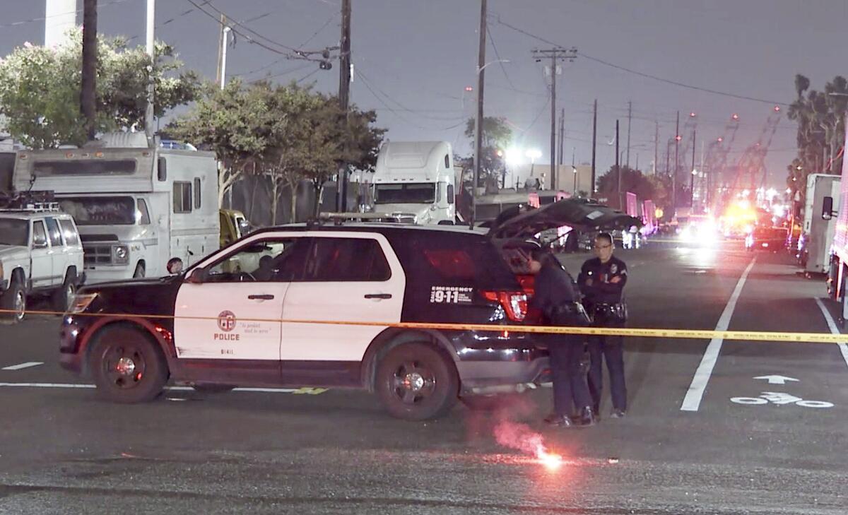 Officers stand next to a patrol car behind police tape.