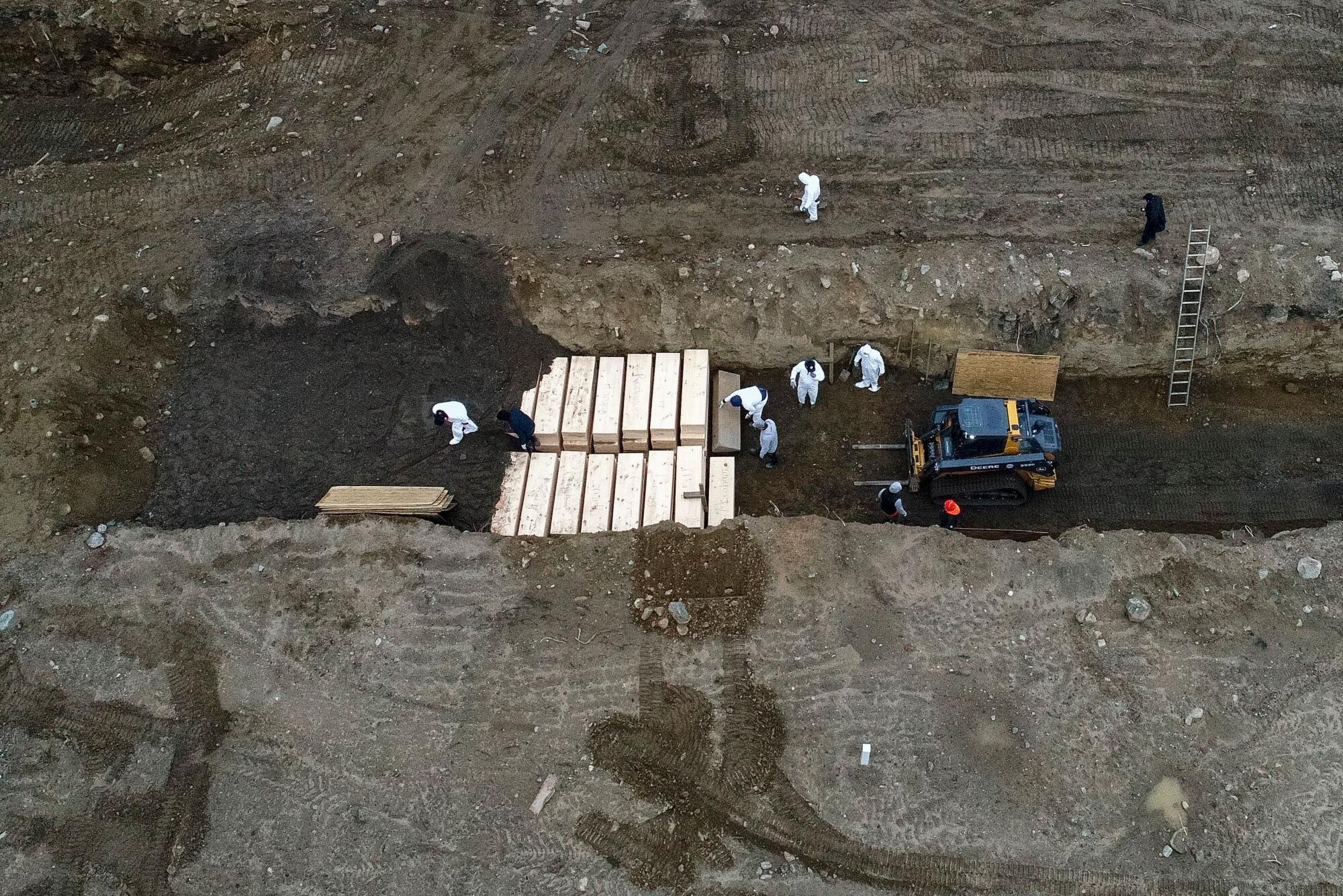 Workers wearing personal protective equipment bury bodies in a trench on Hart Island. 