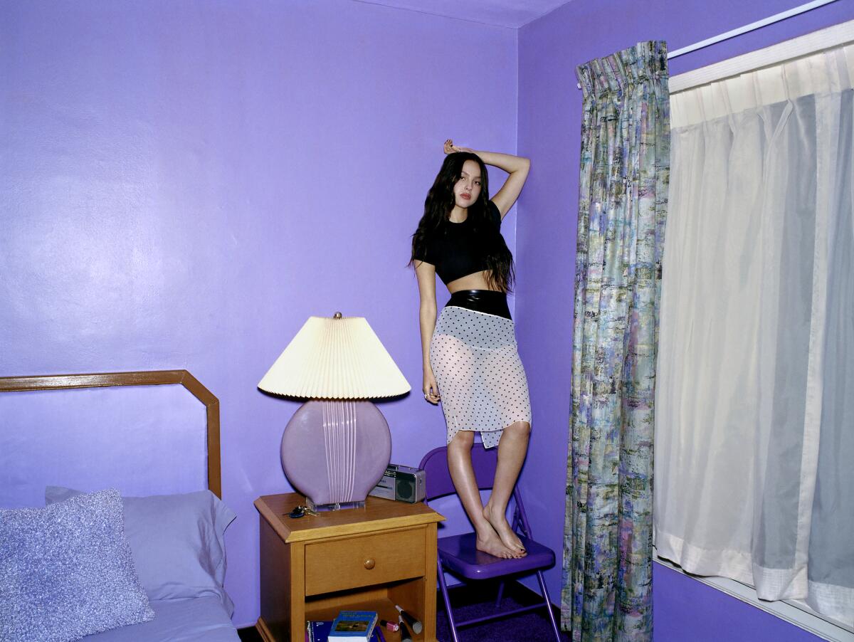 A young woman standing on a folding chair in a bedroom