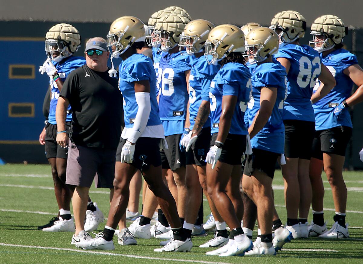 UCLA coach Chip Kelly stands on the field near players during a preseason football practice