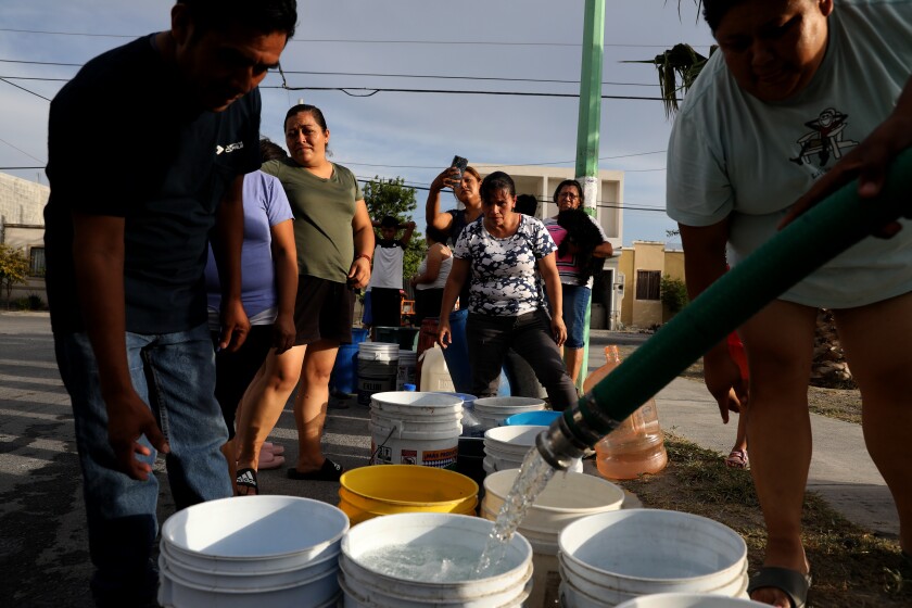 People wait as a hose fill buckets with water.