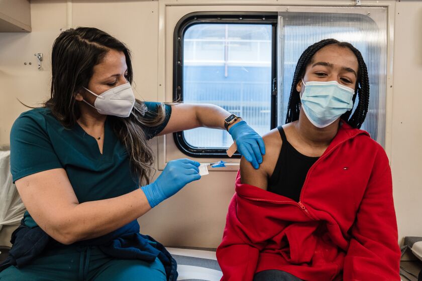 Licensed Vocational Nurse (LVN), Zoe Reza administers the first shot of a vaccine for Covid-19 to Blossom Bess, 15 years, on the UC San Diego Health Mobile Vaccine Clinic at Crawford High School on January 12, 2022.