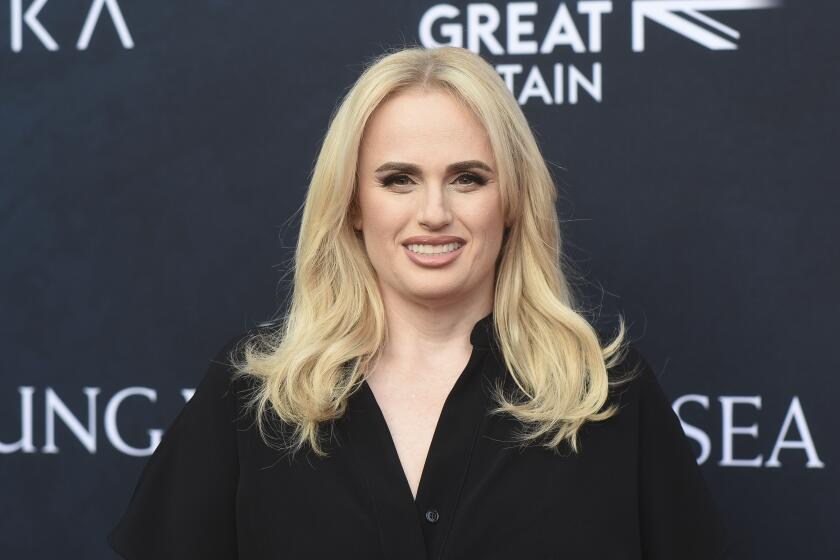 Rebel Wilson smiling with a buss down middle part and black dress. 
