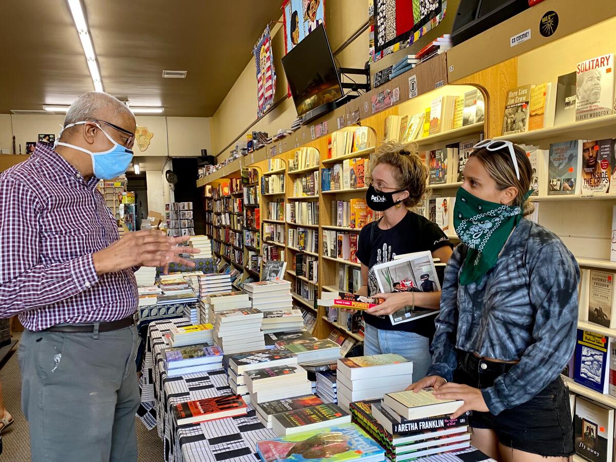  James Fugate speaks with customers across a table covered in stacked books in Eso Won Books