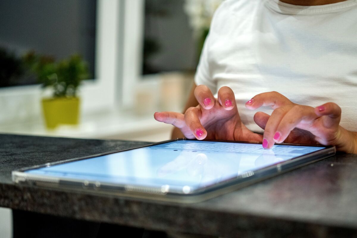 A student with pink nails types on a tablet