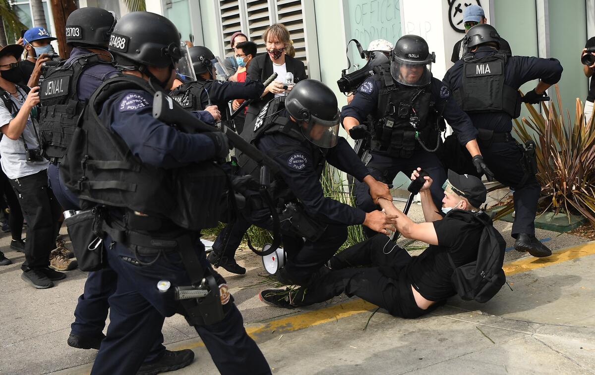 A police officer holds a projectile launcher as others arrest a protester seated on the ground