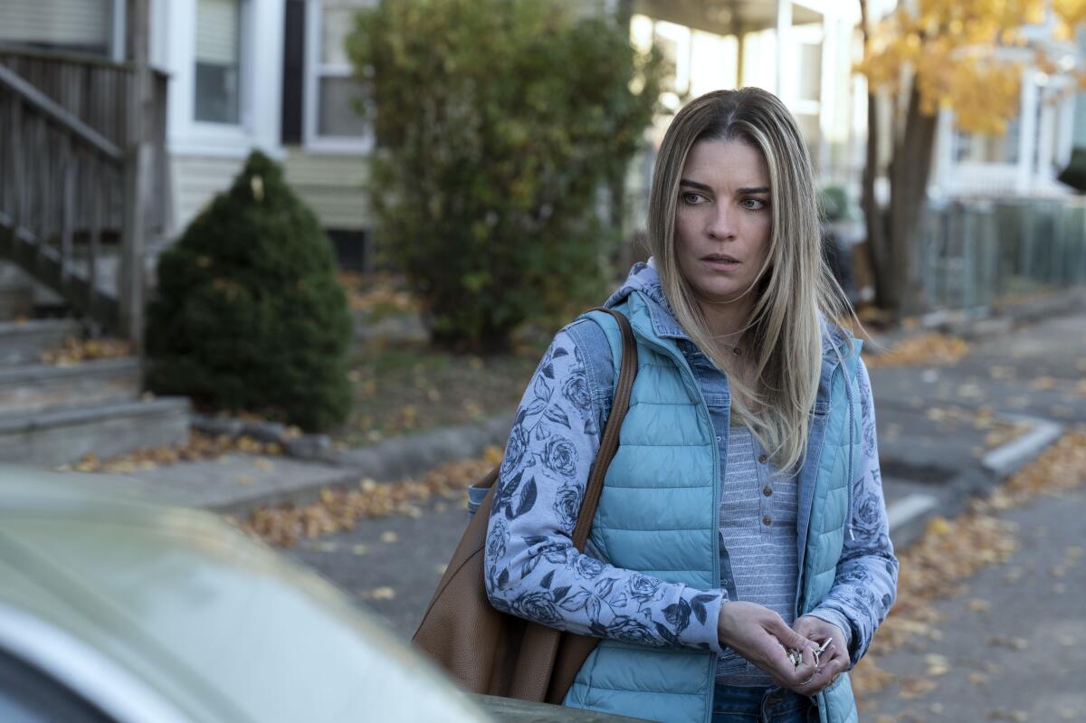 A blond woman in a light blue vest standing on the street holding her car keys