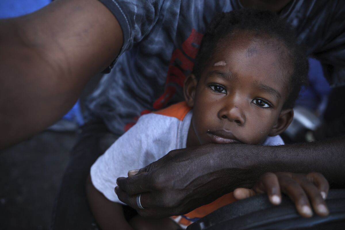 Haitian migrant Dor Louis Hermann holds his three-year-old son Aadam Jr. at a makeshift camp for migrants near El Chaparral pedestrian border bridge in Tijuana, Mexico, Thursday, July 1, 2021. Dor Louis, who left Haiti because of the ongoing violence he allegedly suffered there, has been in Mexico with his family for two years and hopes to cross soon with his family into the United States. (AP Photo/Emilio Espejel)