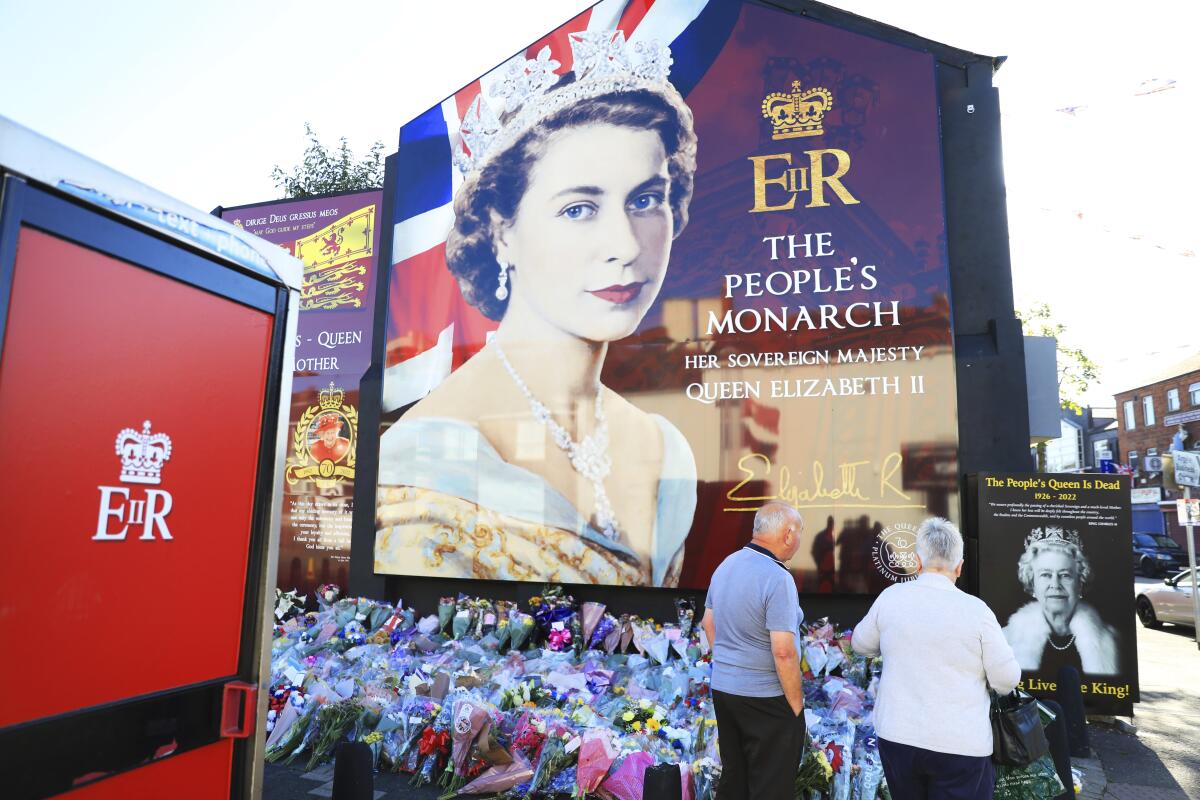 FILE - A couple pay their respect at a picture of Queen Elizabeth II on the Loyalist Shankill Road in west Belfast, Sept. 10, 2022. Britain's longest-reigning monarch and a rock of stability across much of a turbulent century, died Sept. 8, 2022. (AP Photo/Peter Morrison, File)