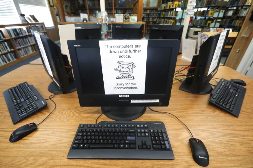 FILE - In this Aug. 22, 2019, file photo, signs on a bank of computers tell visitors that the machines are not working at the public library in Wilmer, Texas. Some cybersecurity professionals are concerned that insurance policies designed to limit the damage of ransomware attacks might actually be encouraging hackers. Twenty-two local governments in Texas were hit in August. (AP Photo/Tony Gutierrez, File)