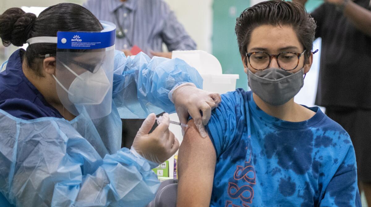 A person in a face mask and shield vaccinates another person.