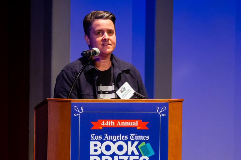A woman in a black T-shirt and black jacket stands at a lectern with the Los Angeles Times Book Prizes logo.