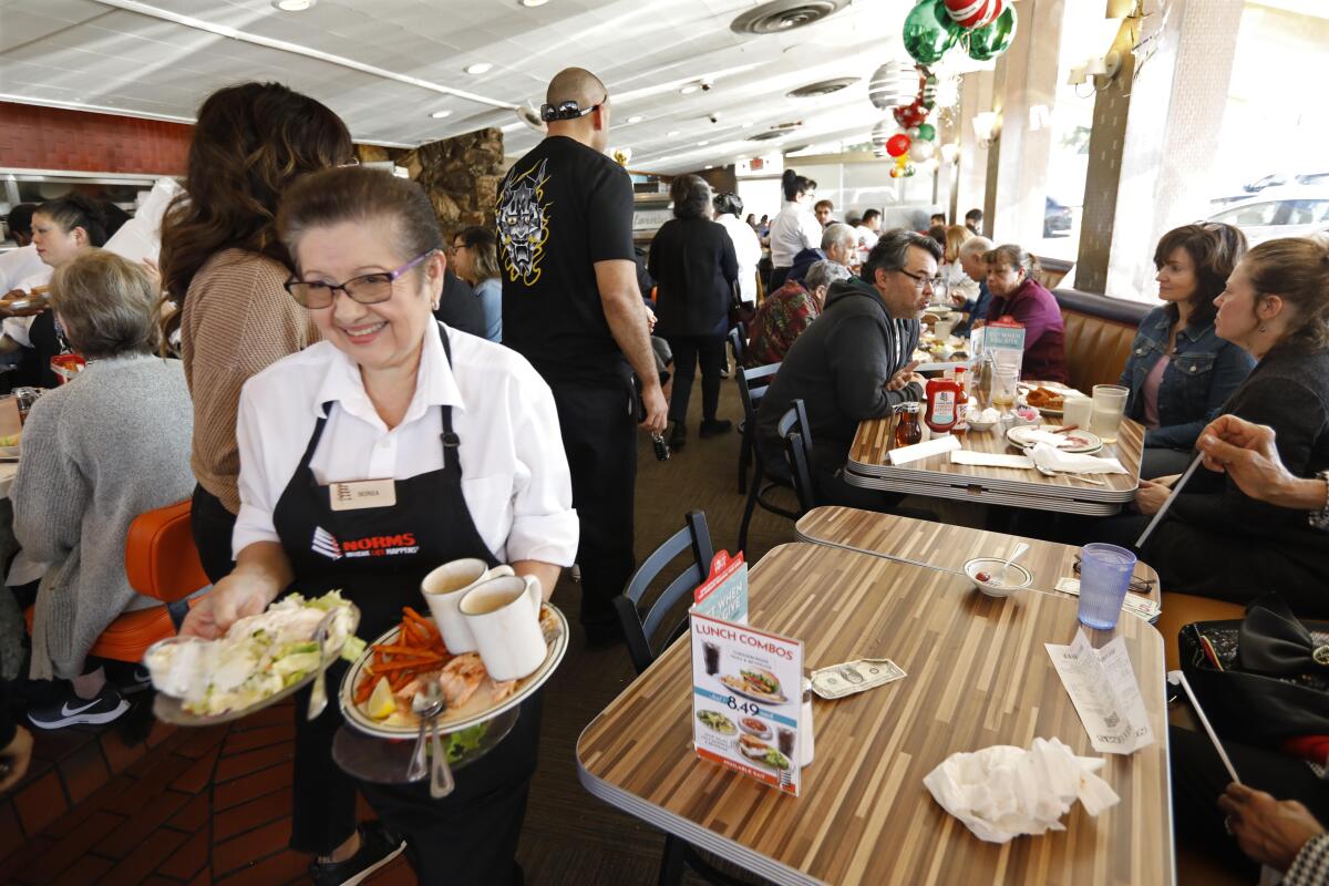 Waitress Sonia Bernal clears plates from a table at Norms in West Hollywood.