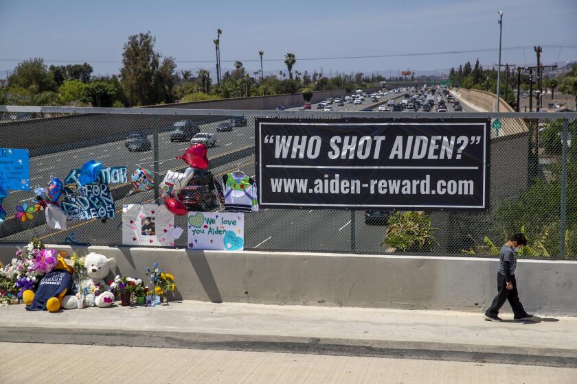 Orange, CA - May 27: Six-year-old Victor Flores, of Orange, walks alone clutching a Pokemon card for comfort, ahead of his family, where his dad said he was sad because he is the same age as 6-year-old shooting victim Adrian Leos, where they prayed and left flowers at a growing makeshift memorial on the Walnut Ave. overpass of the 55 Freeway in Orange May 27, 2021. The memorial featured balloons, toys, cards, messages of love and candles to remember a 6-year-old boy who was shot and killed Friday during an apparent road rage incident on the 55 Freeway. New banners have been placed on the overpass as officials and community continue to increase the reward for arrest of the killer and accomplice. (Allen J. Schaben / Los Angeles Times)