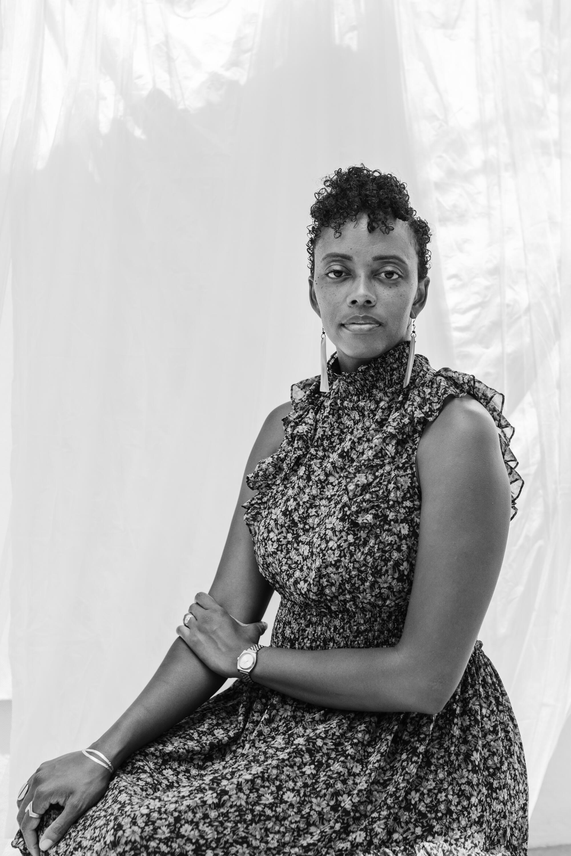 A black and white portrait of writer Angela Flournoy wearing a floral dress sitting in front of a fabric backdrop