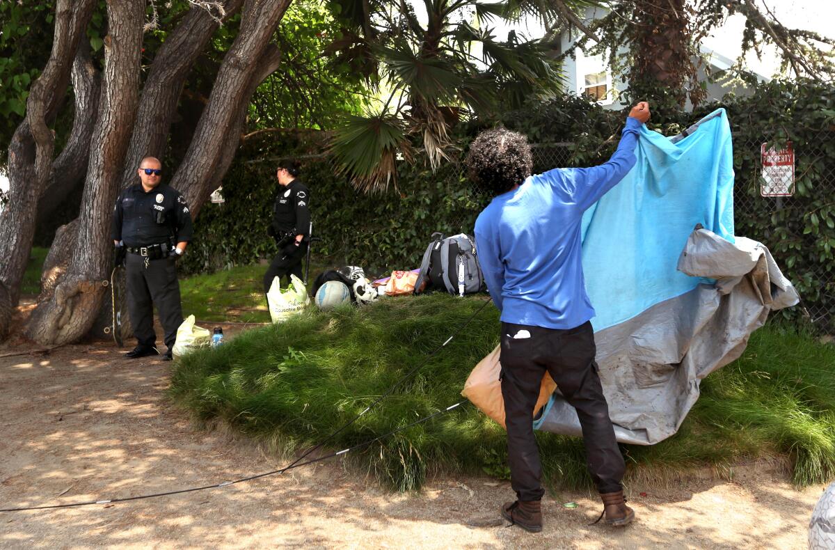 Police officers watch as a homeless man collects his belongings