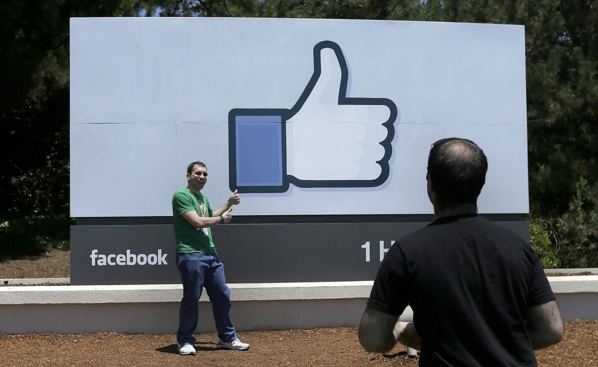 A man poses for photographs in front of the Facebook sign on the company's campus in Menlo Park, Calif.