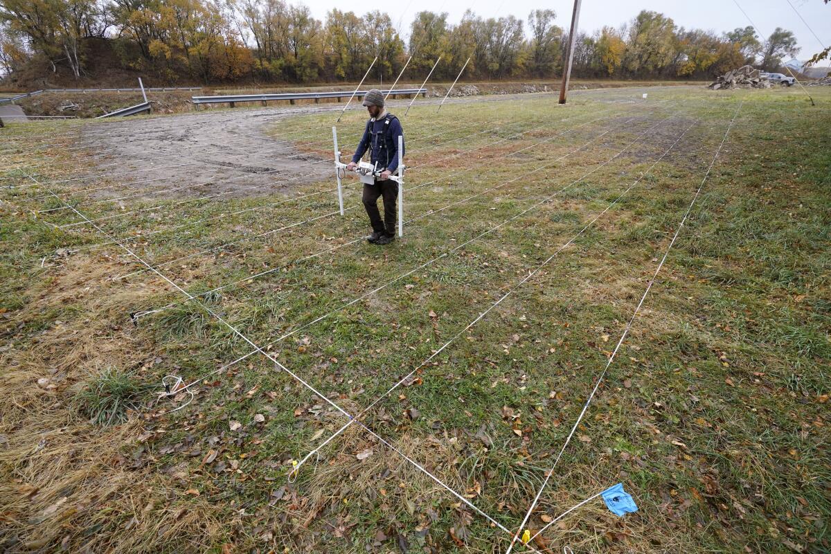 A man uses ground-penetrating radar equipment to scan a piece of land marked out in a grid using string