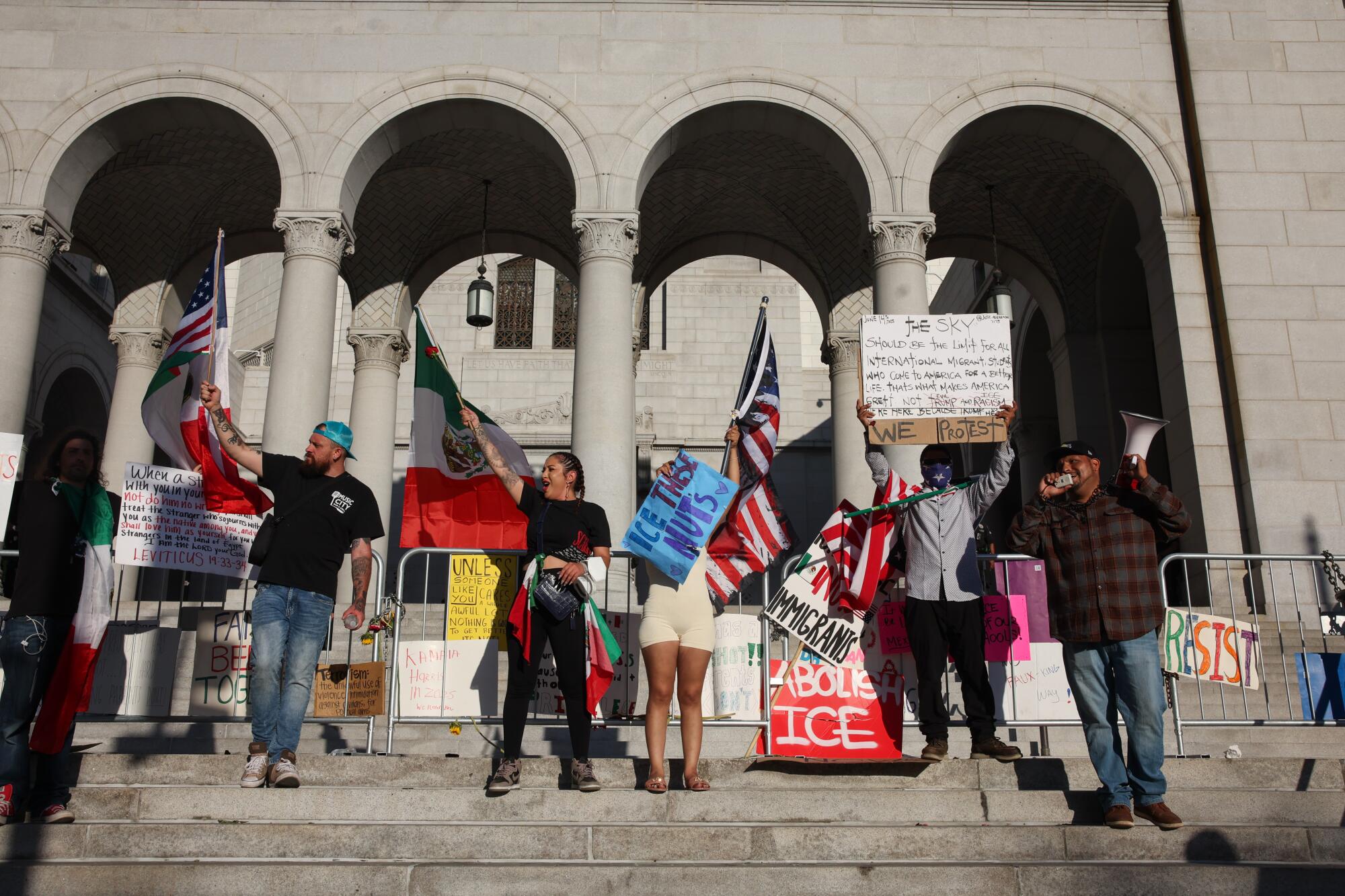 A group of protesters hold signs and wave flags on the steps of a building.