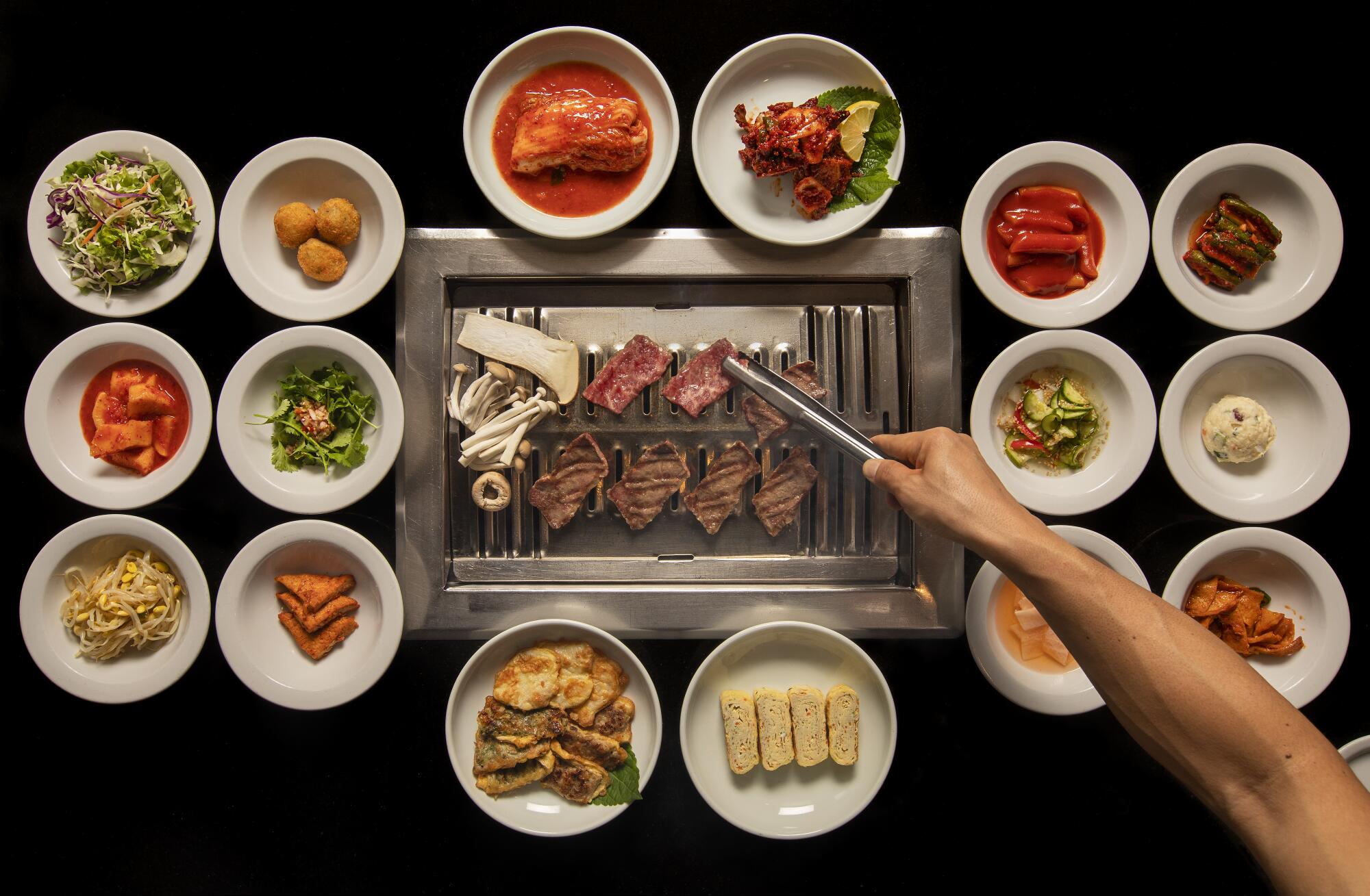 Meat on a tabletop grill surrounded by small white dishes of assorted banchan at Park's BBQ.