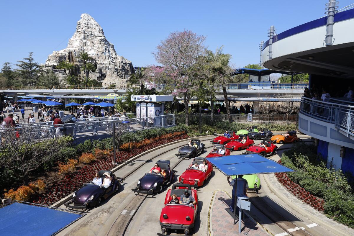 Disneyland guests wait in traffic near the exit to Autopia, with the Matterhorn Bobsleds ride in the background.