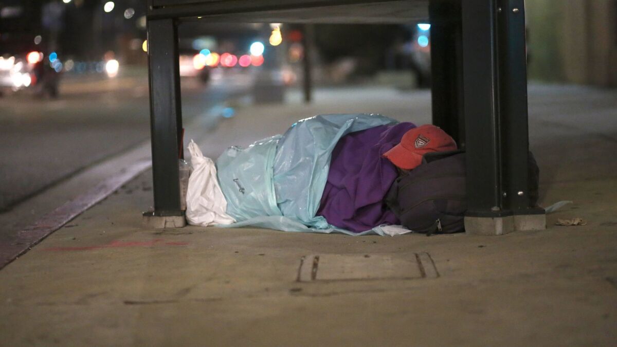 A homeless person sleeps wrapped in plastic bags on Hollywood Boulevard.