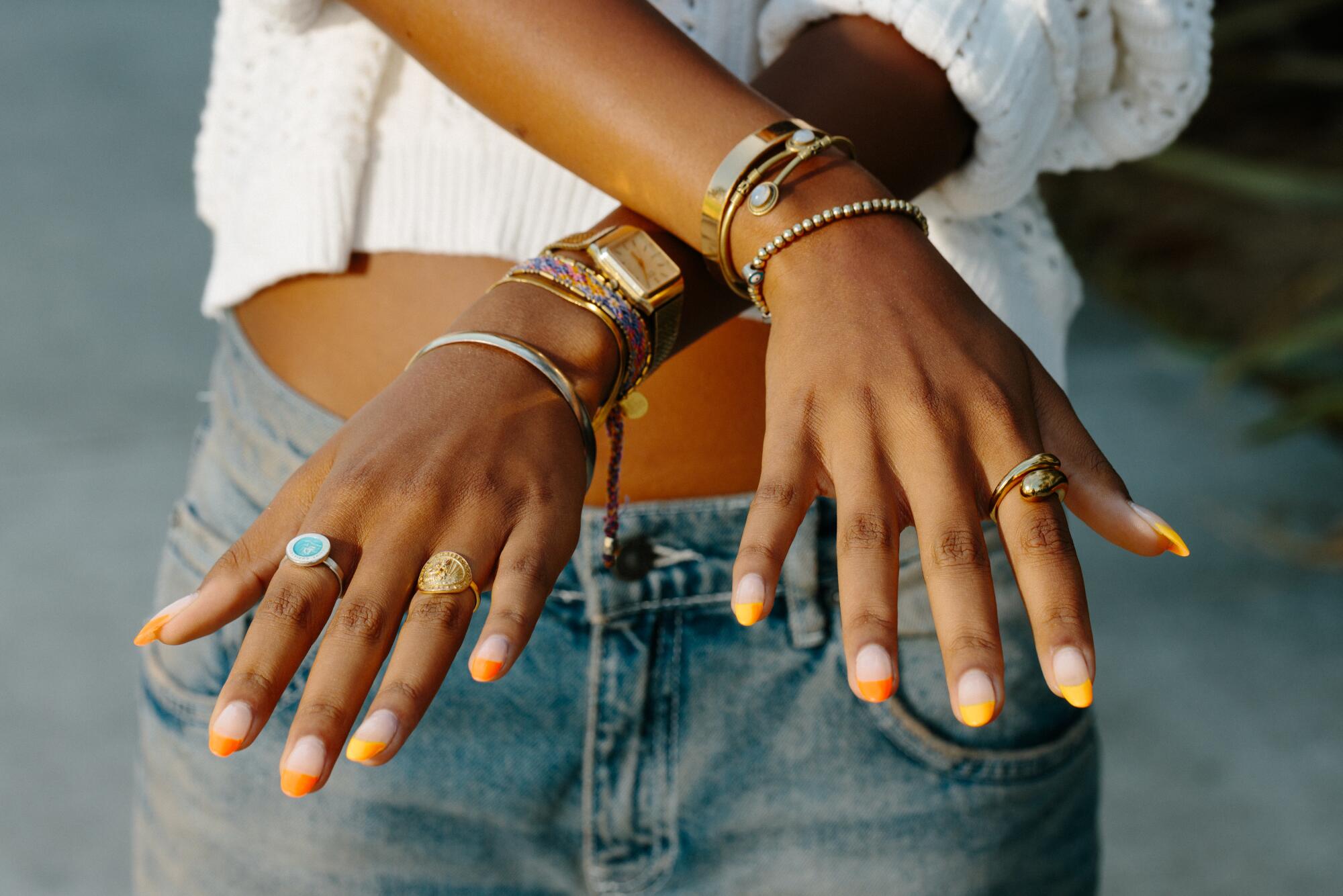 A pair of hands, wearing rings and bracelets and styled with orange French-tipped nails.