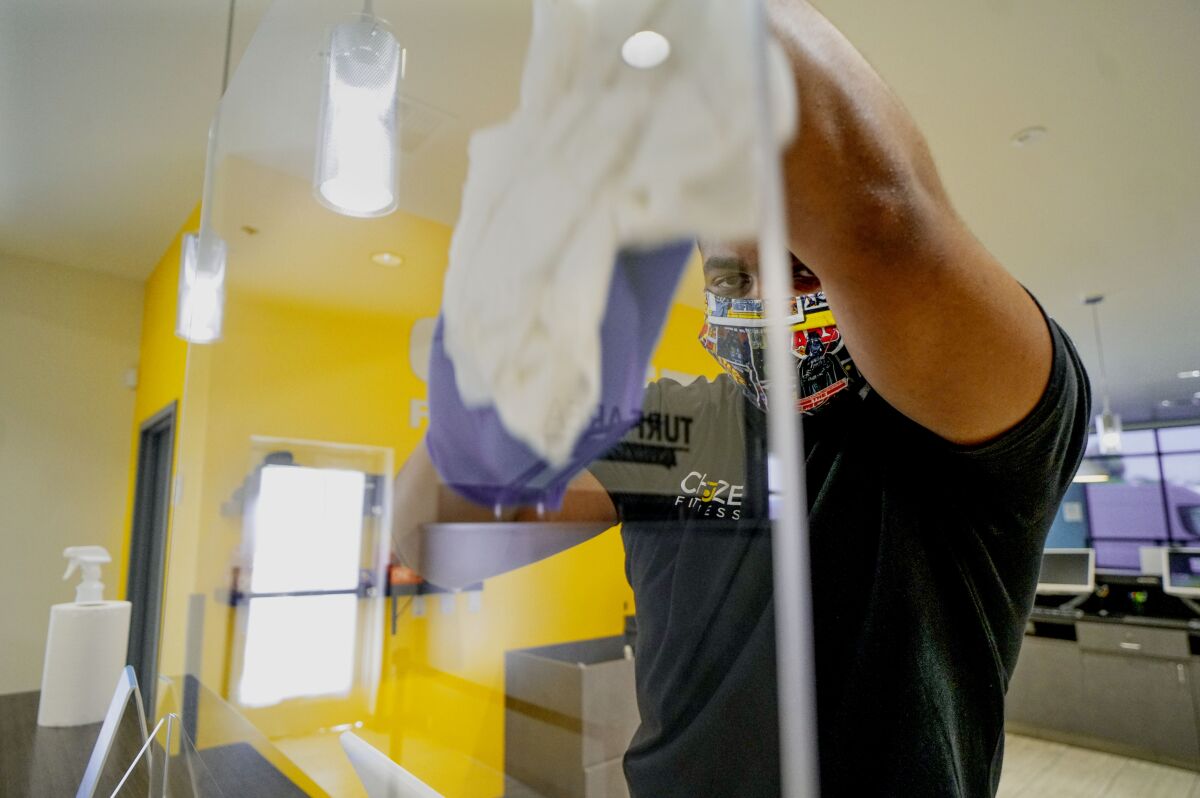 Employee Nijal Collins wipes down a plastic shield at the register at Chuze Fitness in Chula Vista.
