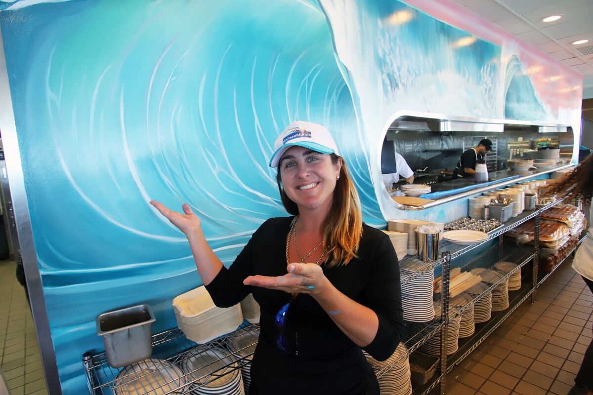 Melissa Murphy, a Huntington Beach muralist, poses with a mural she painted that decorates the kitchen at Bud & Gene's.
