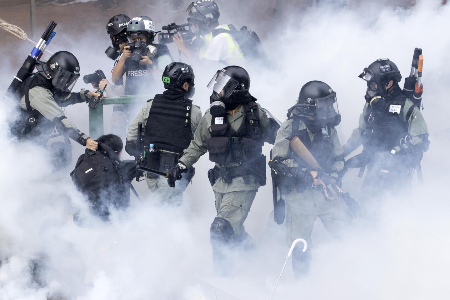 Police in riot gear move through a cloud of smoke as they detain a protestor at the Hong Kong Polytechnic University in Hong Kong, Monday, Nov. 18, 2019. Hong Kong police fought off protesters with tear gas and batons Monday as they tried to break through a police cordon that is trapping hundreds of them on a university campus. (AP Photo/Ng Han Guan)