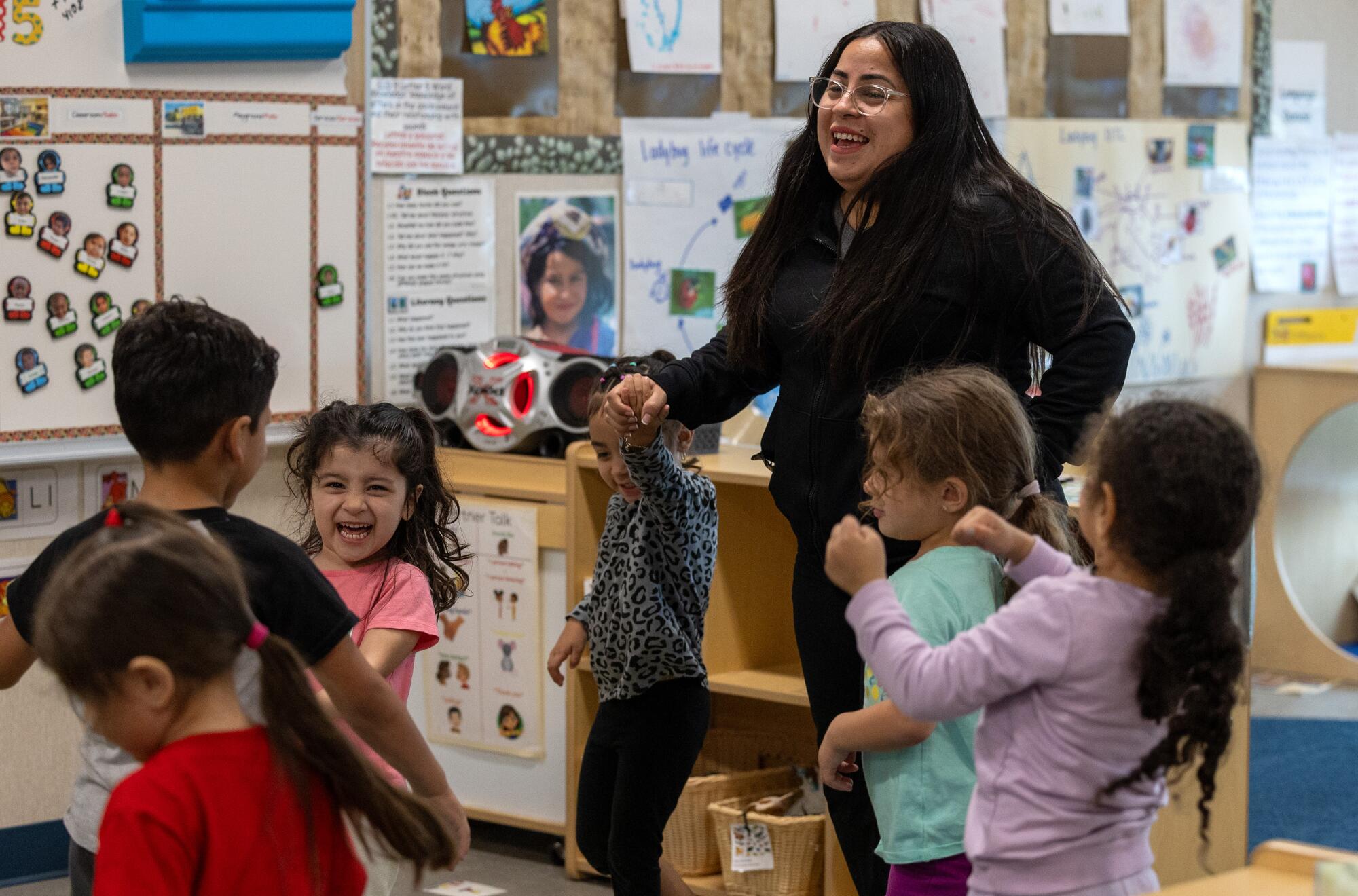 A woman dances with young children in a classroom.