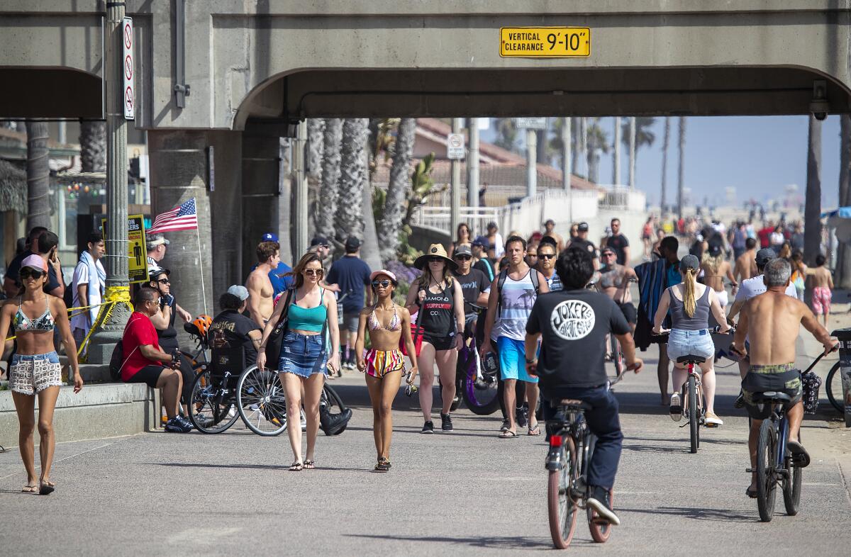 People crowd the bike path around the Huntington Beach pier April 25. Many donned hats, sunglasses and umbrellas, and some brought hand sanitizer, but few wore protective masks.